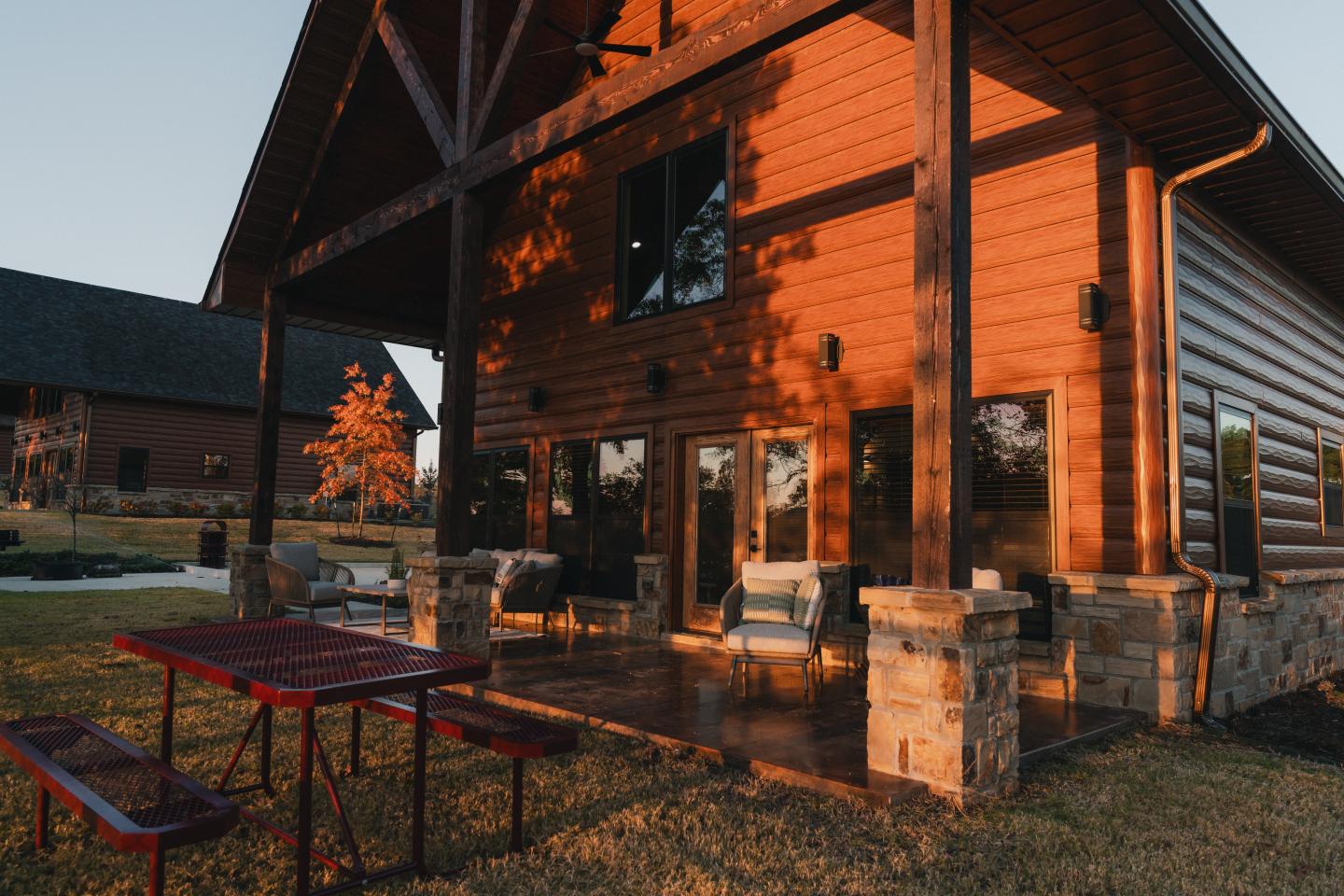 Rustic wooden cabin at sunset with a porch and red picnic table.