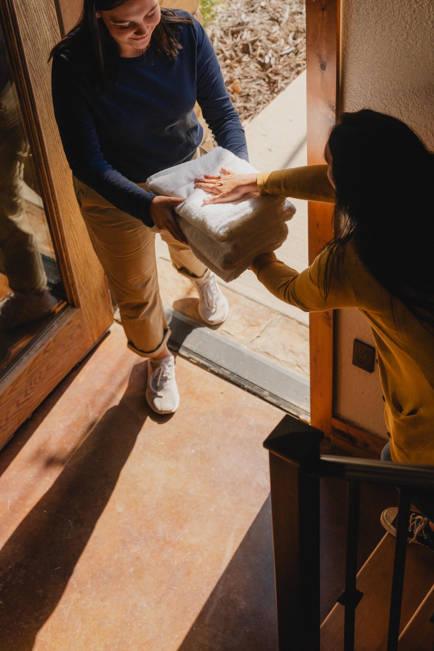 Two people exchange a package at a doorway, sunlight streaming in.