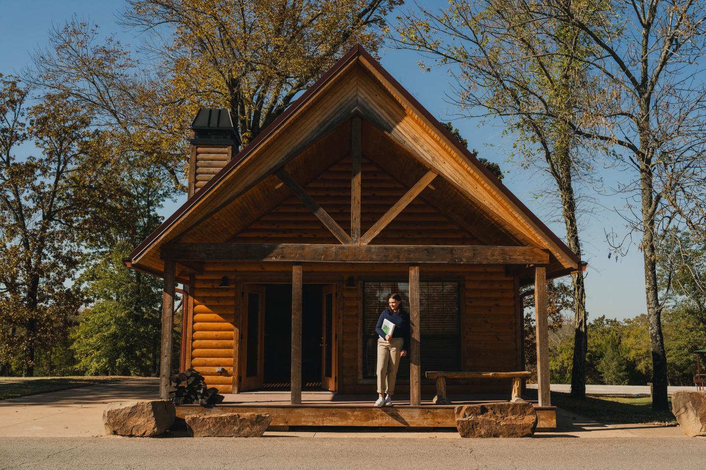 Rustic log cabin surrounded by fall trees under a clear blue sky.