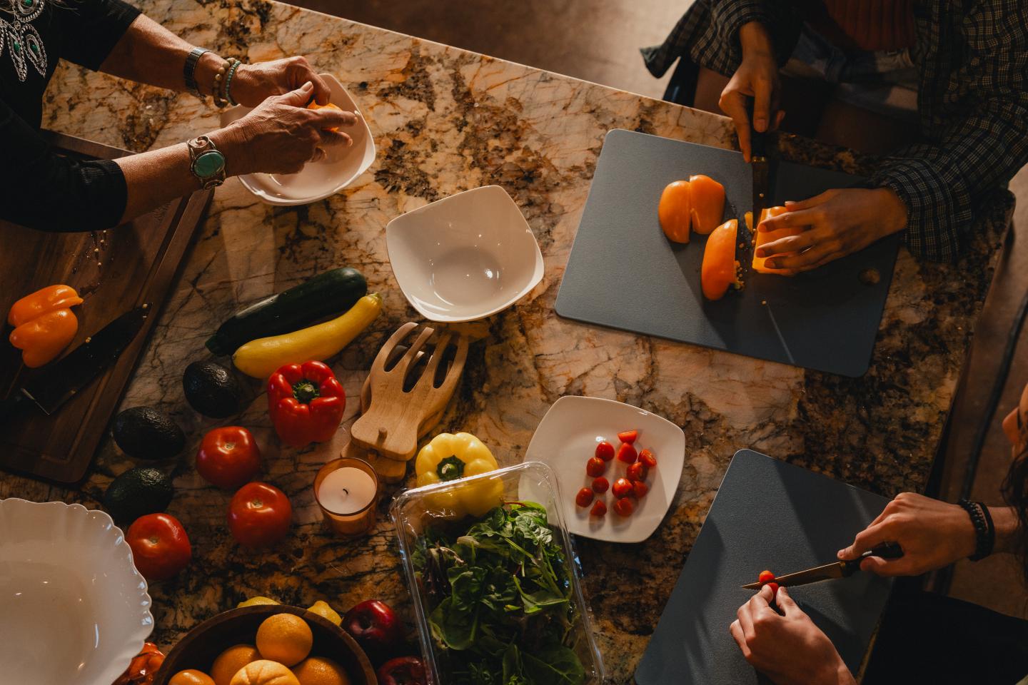 People preparing vegetables on a kitchen counter, surrounded by produce.