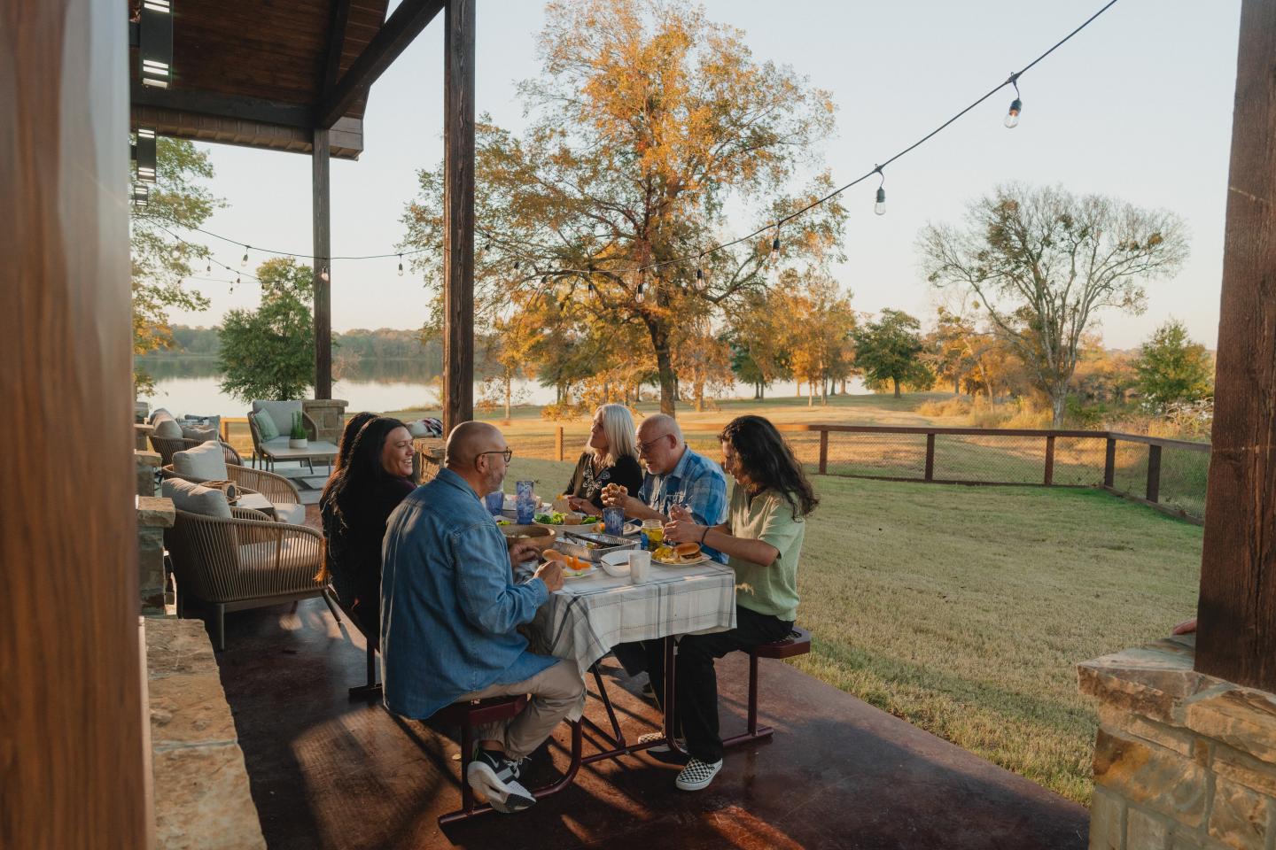 Family dining outdoors on a patio, surrounded by trees and a grassy lawn.