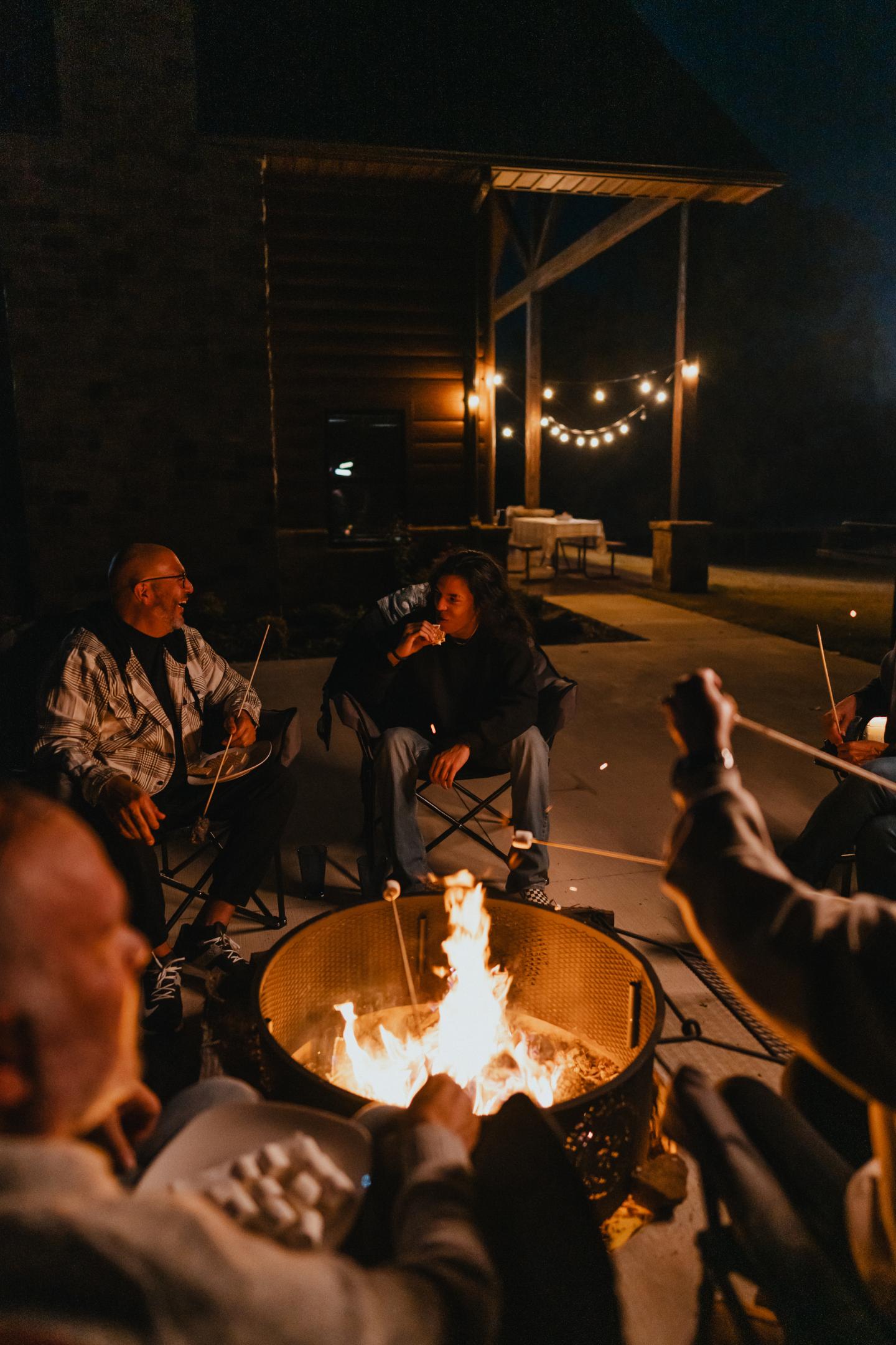 People sitting around a campfire at night, with warm lighting and a cozy atmosphere.