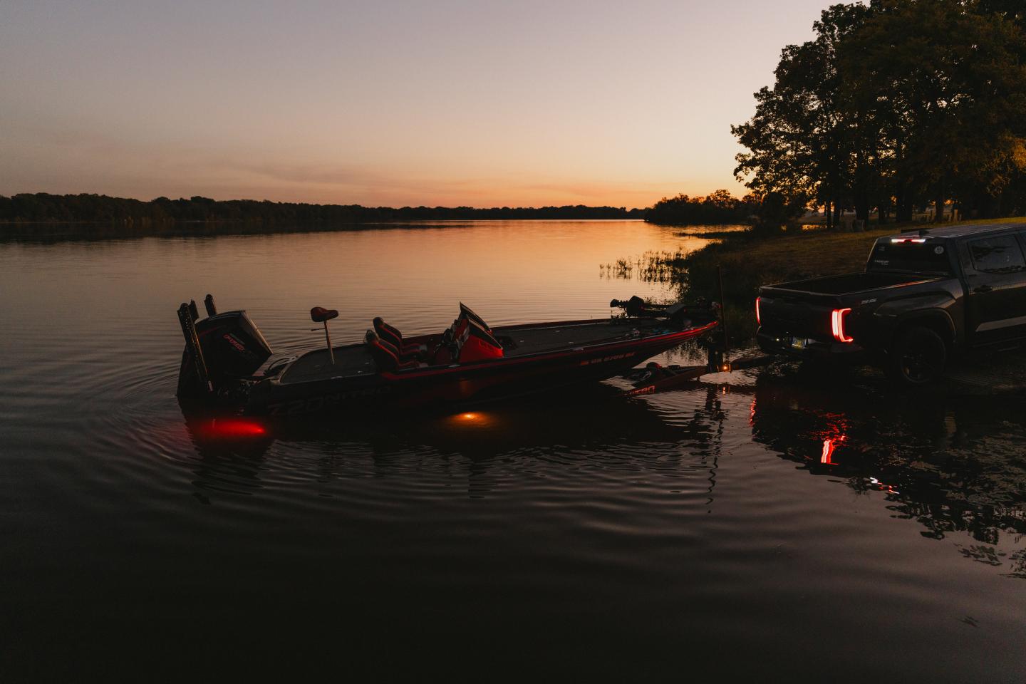 Boat being towed from lake at sunset with glowing red lights.