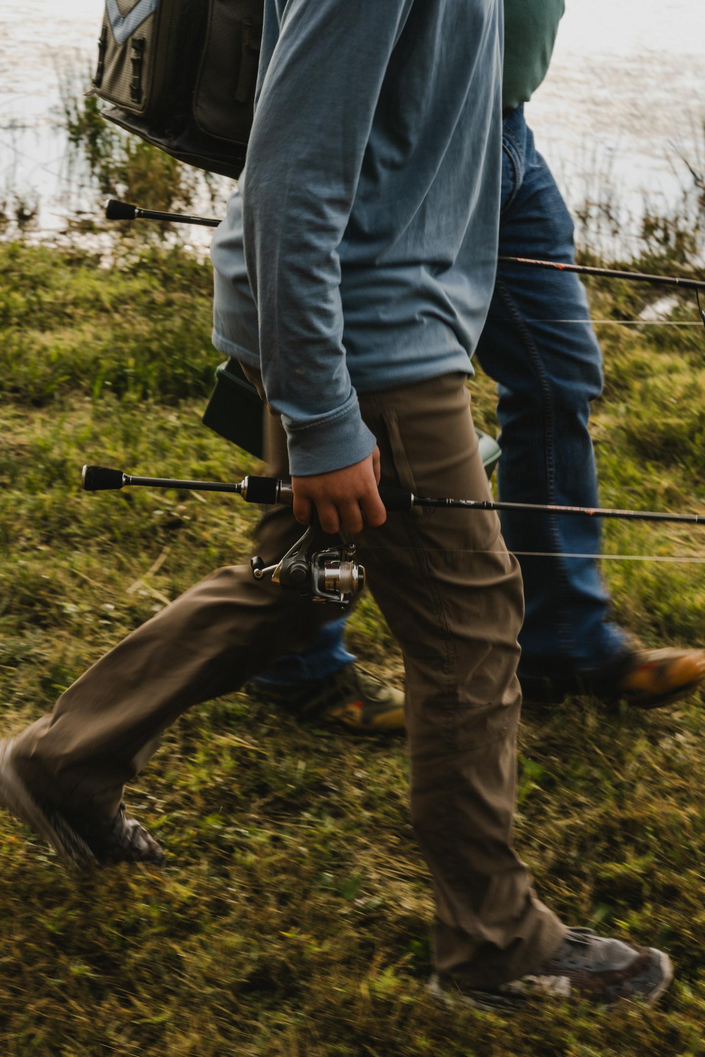 Two people walking on grass, one carrying fishing rods.