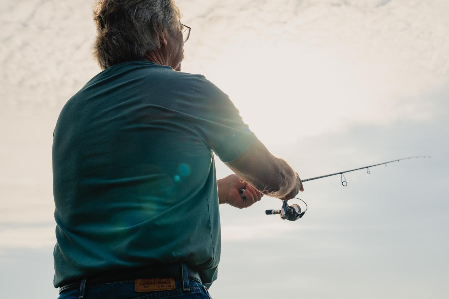 Man fishing under a cloudy sky, holding a rod.