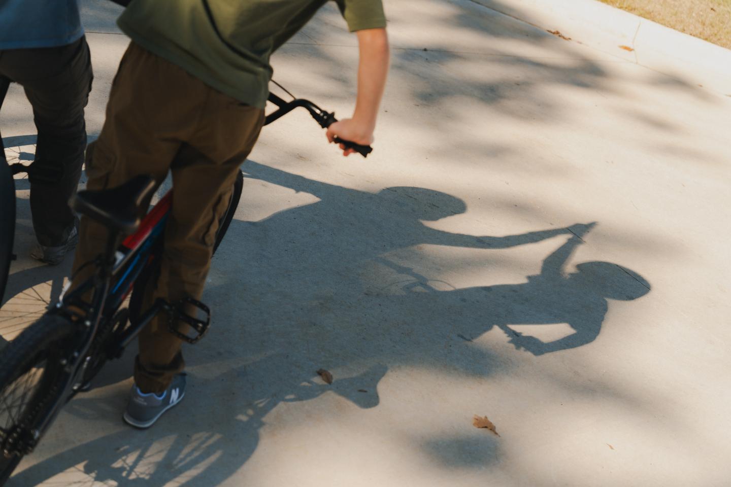 Boy on a bicycle casts a shadow on a sunlit pavement.