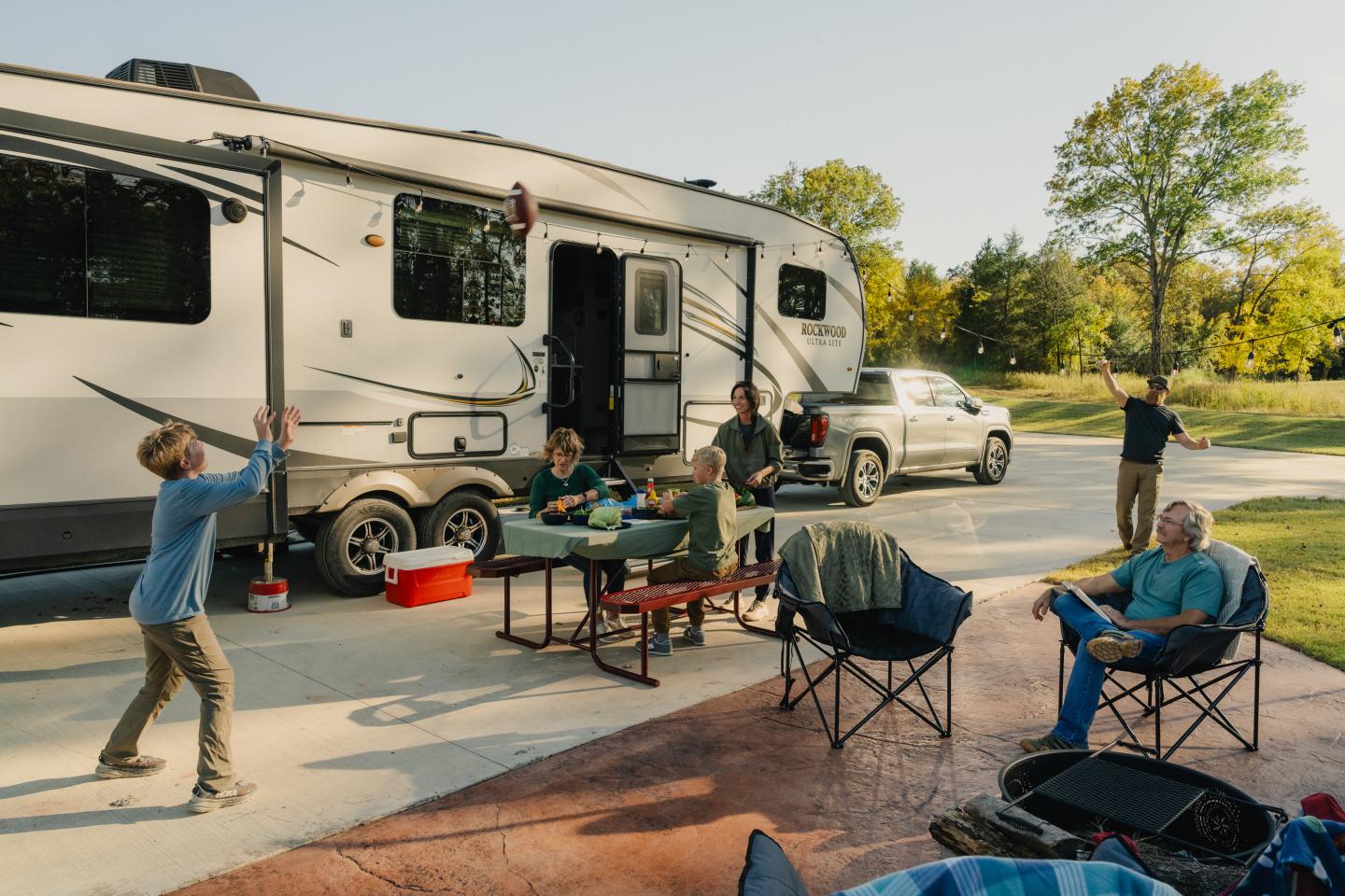 Family enjoying time outside an RV in a sunny park setting.