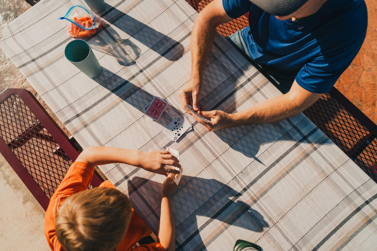 Two people playing cards at a sunlit picnic table.