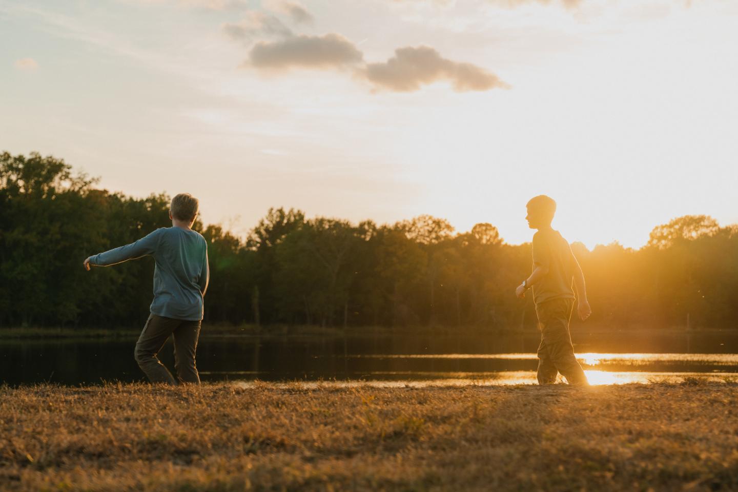 Two people walking by a lake at sunset with trees in the background.