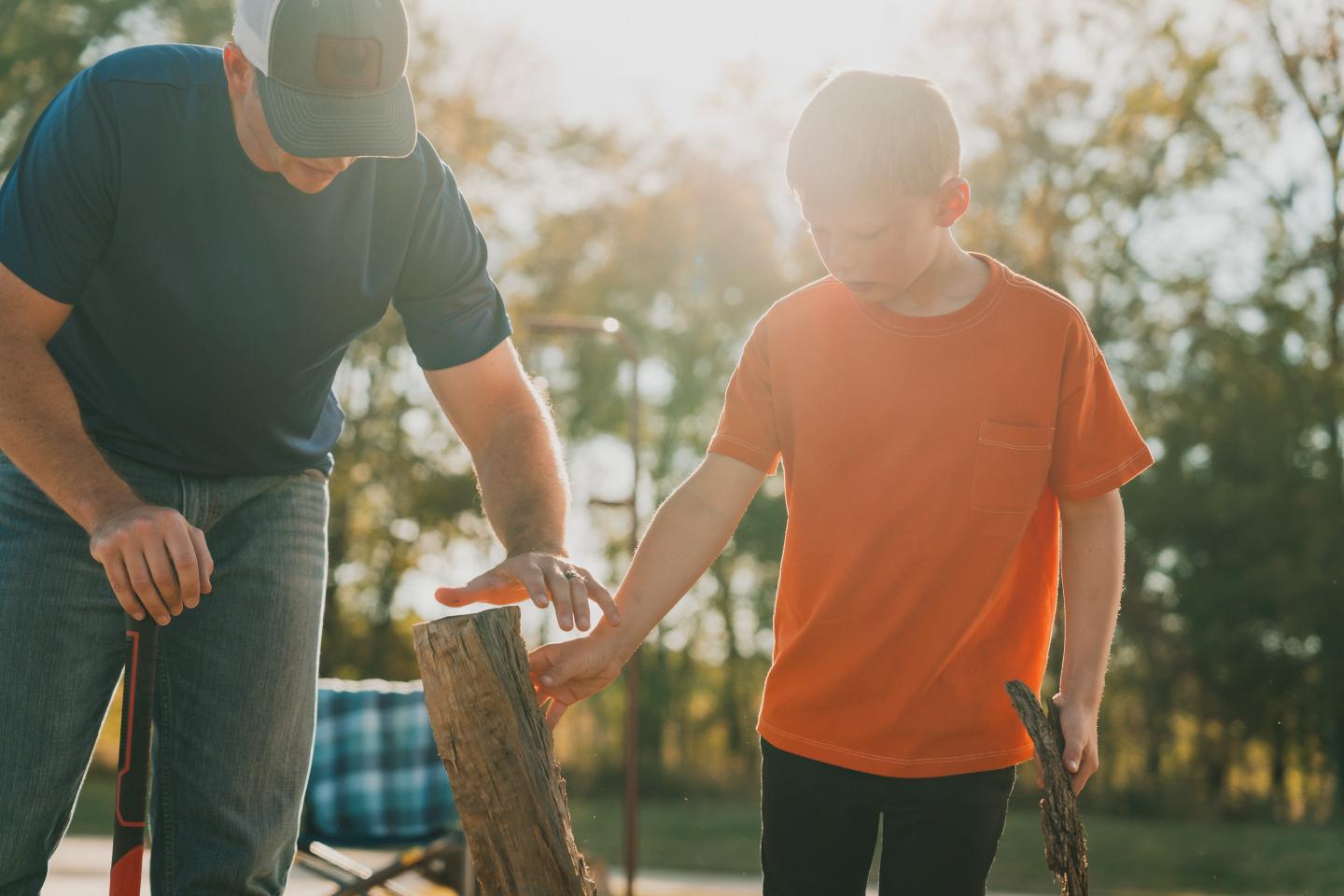 Man and boy outdoors, chopping wood, sunlit background.