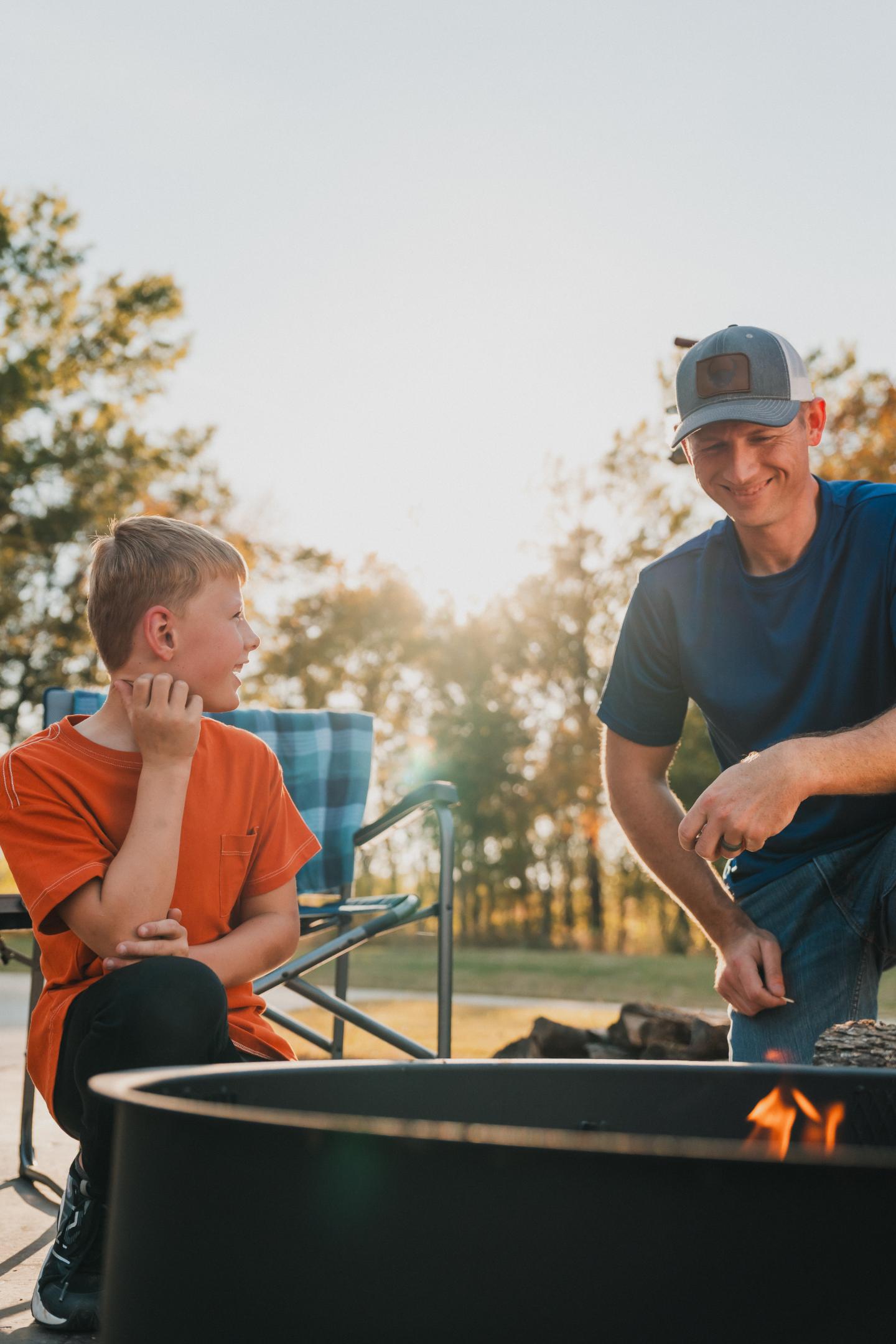 Boy and man by a campfire, smiling at sunset.