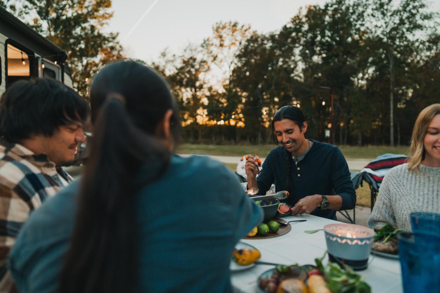 Group enjoying an outdoor meal at sunset, surrounded by trees.
