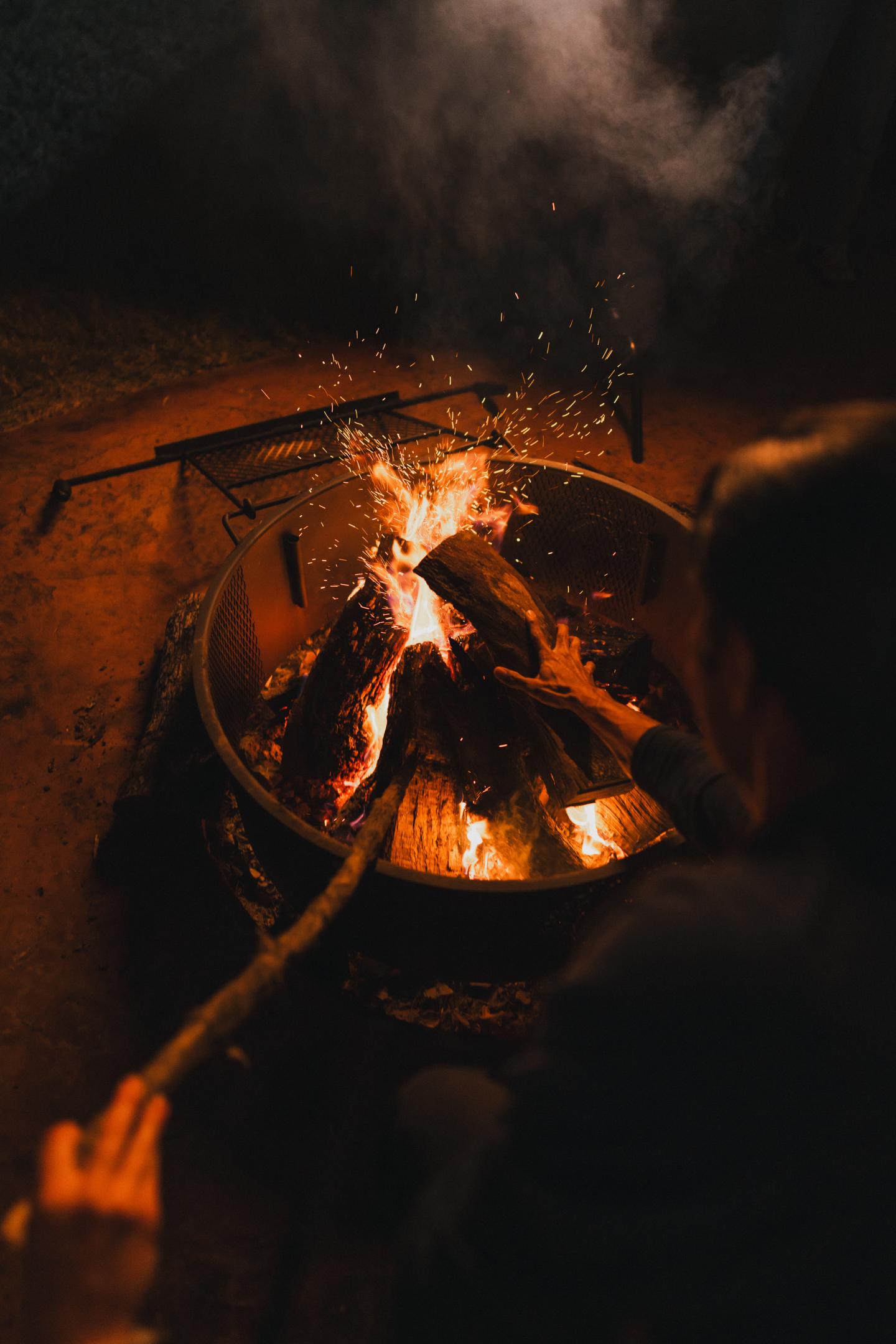 Campfire at night with two people adding wood.