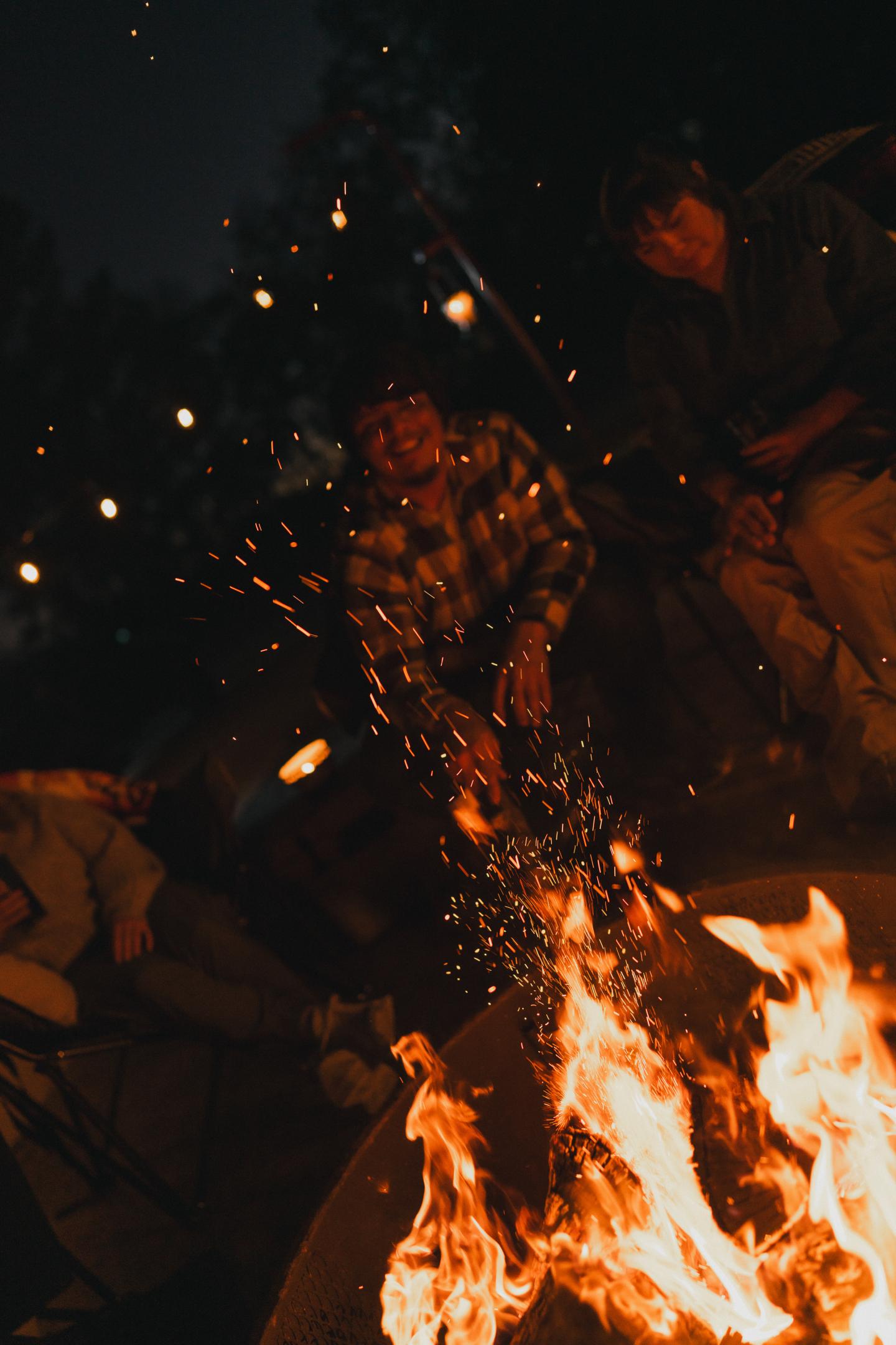 Campfire with people sitting around at night, sparks flying.