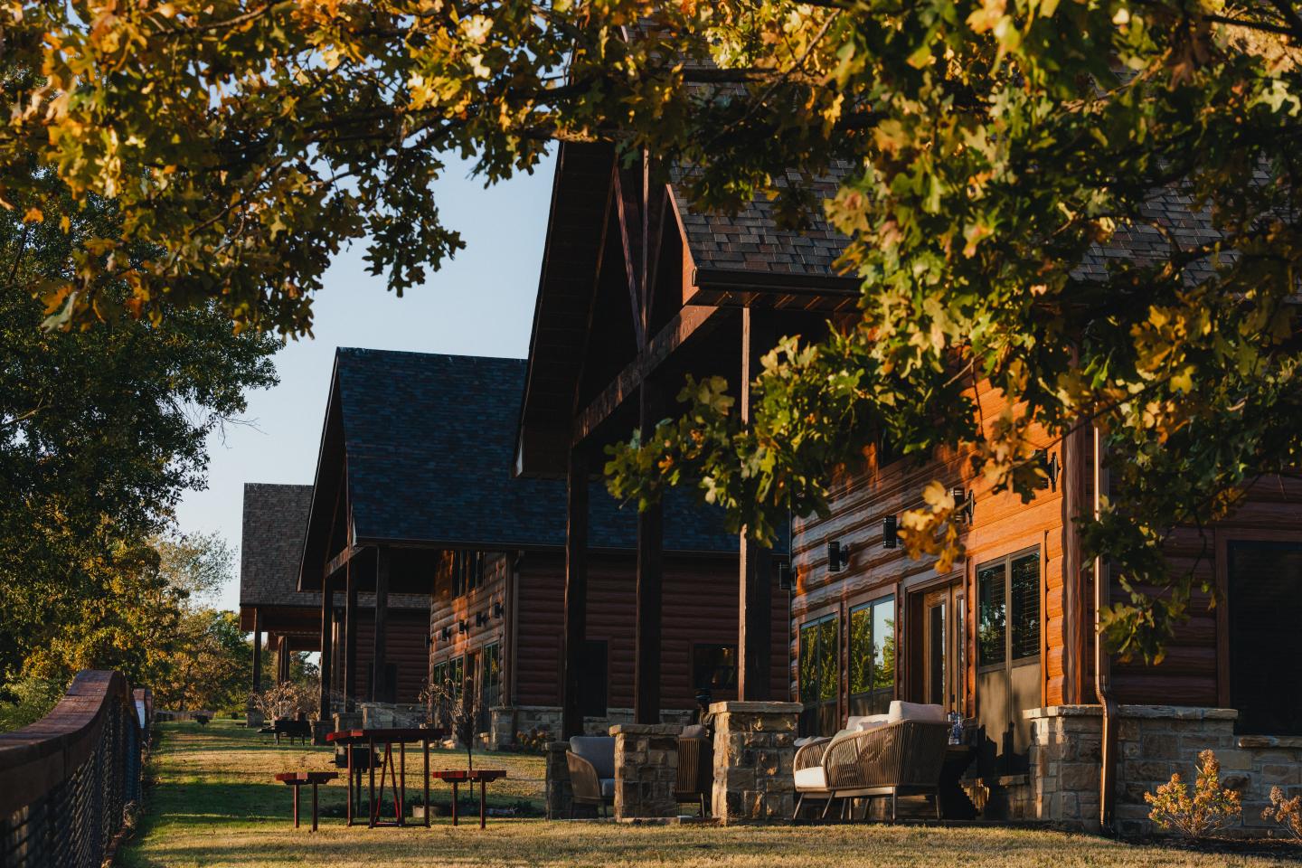 Wooden cabins lined under autumn trees in warm sunlight.