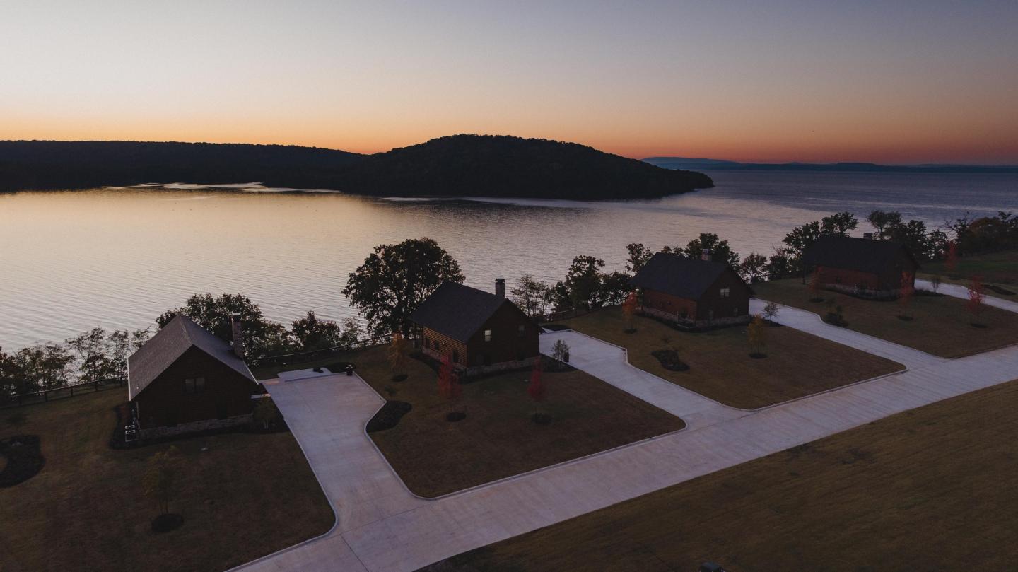 Four cabins by a lake at sunset, surrounded by trees.