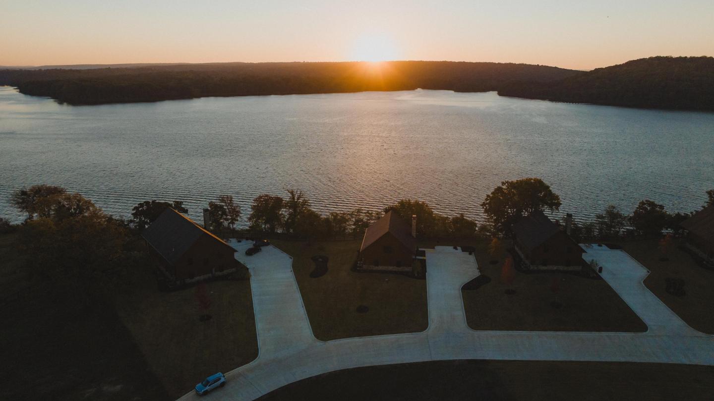 Sunset over a tranquil lake with houses and driveways in the foreground.