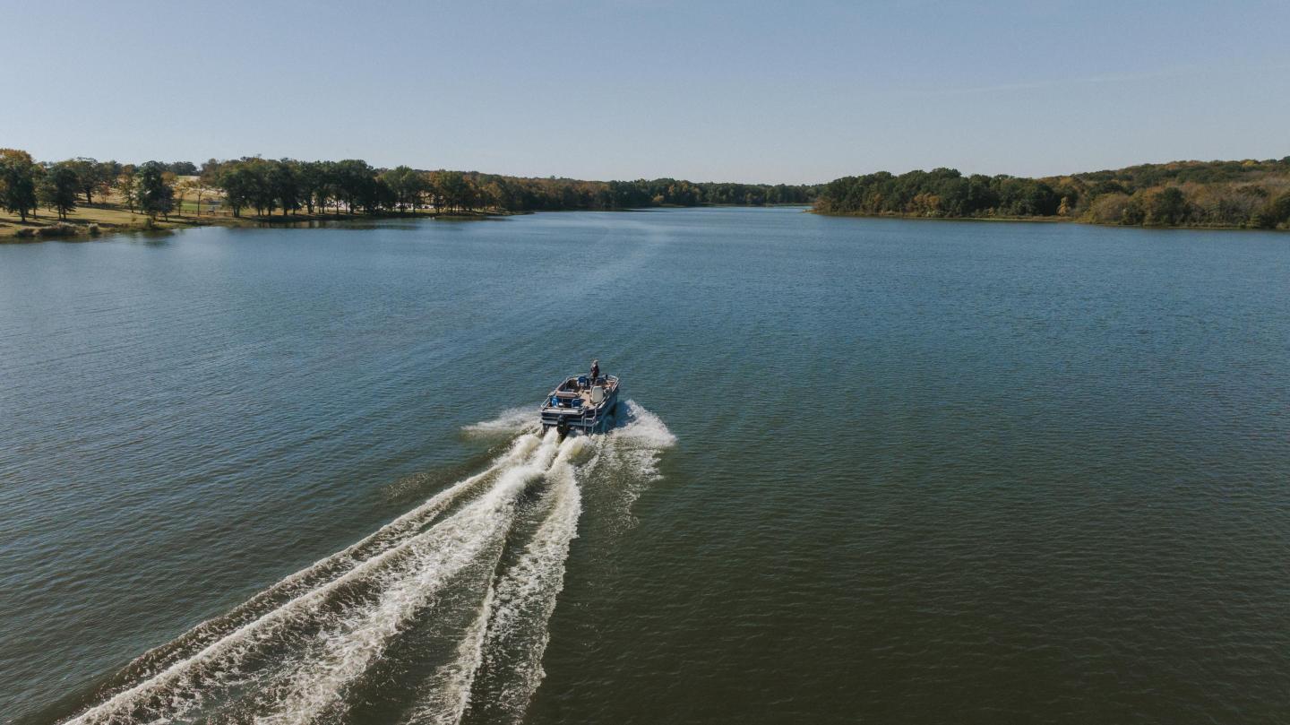 Boat speeding on a wide river under a clear blue sky.