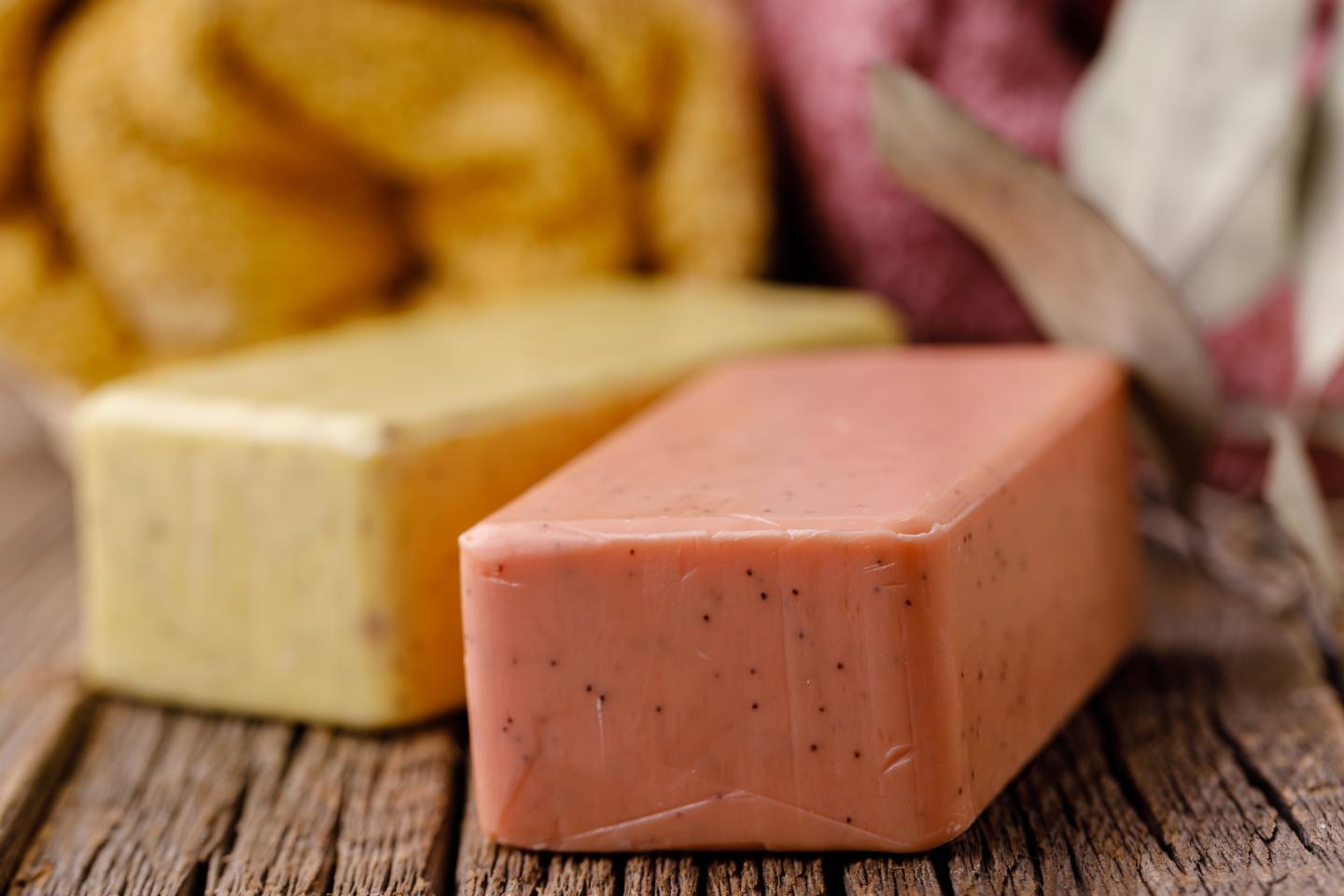 Two bars of soap, one pink, one yellow, on a wooden surface with towels.