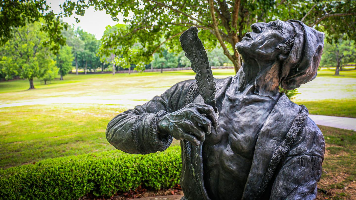 Bronze statue of a man gazing upwards in a lush park.