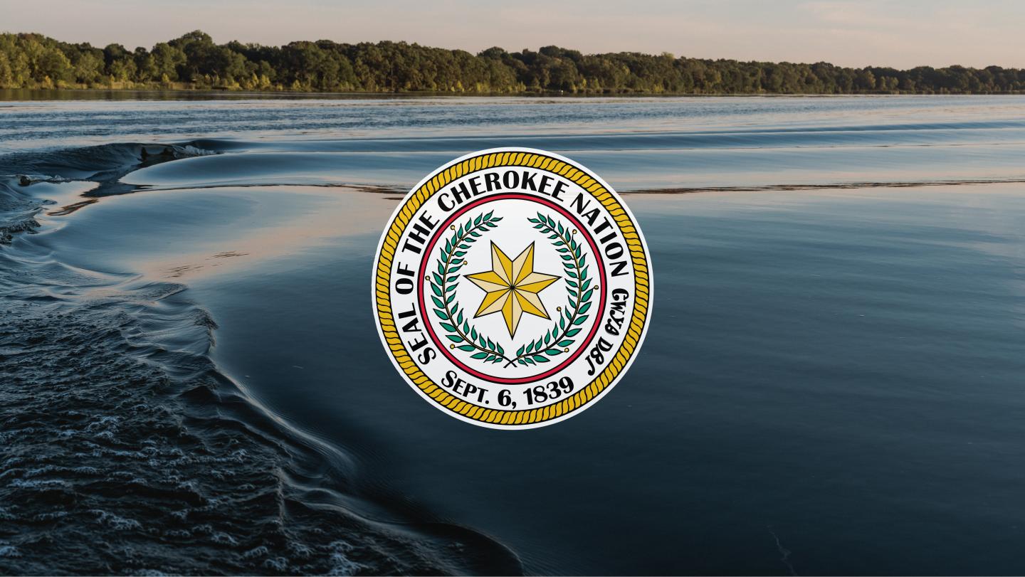 Seal of the Cherokee Nation over a serene lake and forest backdrop.