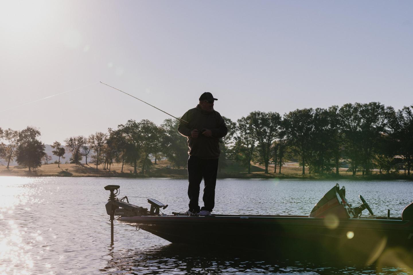 Silhouette of a person fishing on a boat at sunrise.