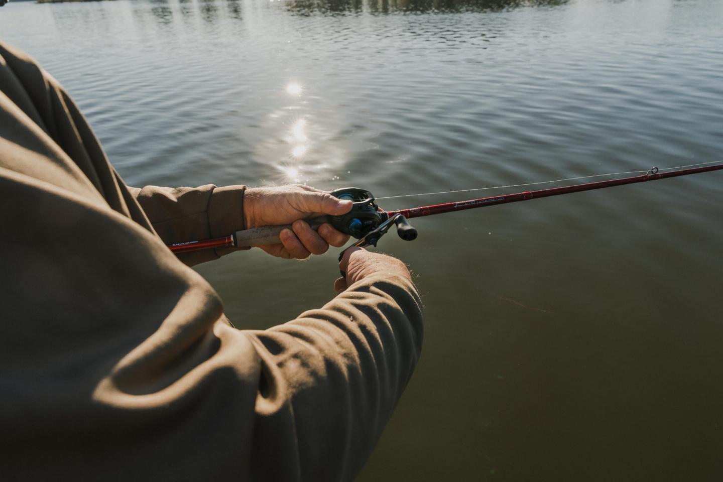 A person fishing in a lake, wearing a brown jacket, holding a fishing rod.