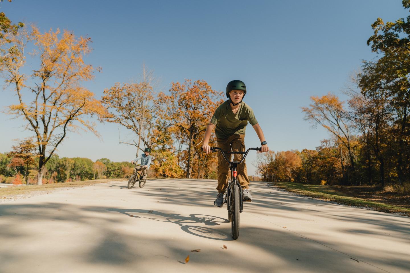 Boy cycling on a path, surrounded by autumn trees under a clear blue sky.