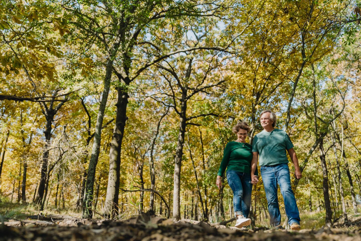 Couple walking in a sunlit forest with autumn leaves.