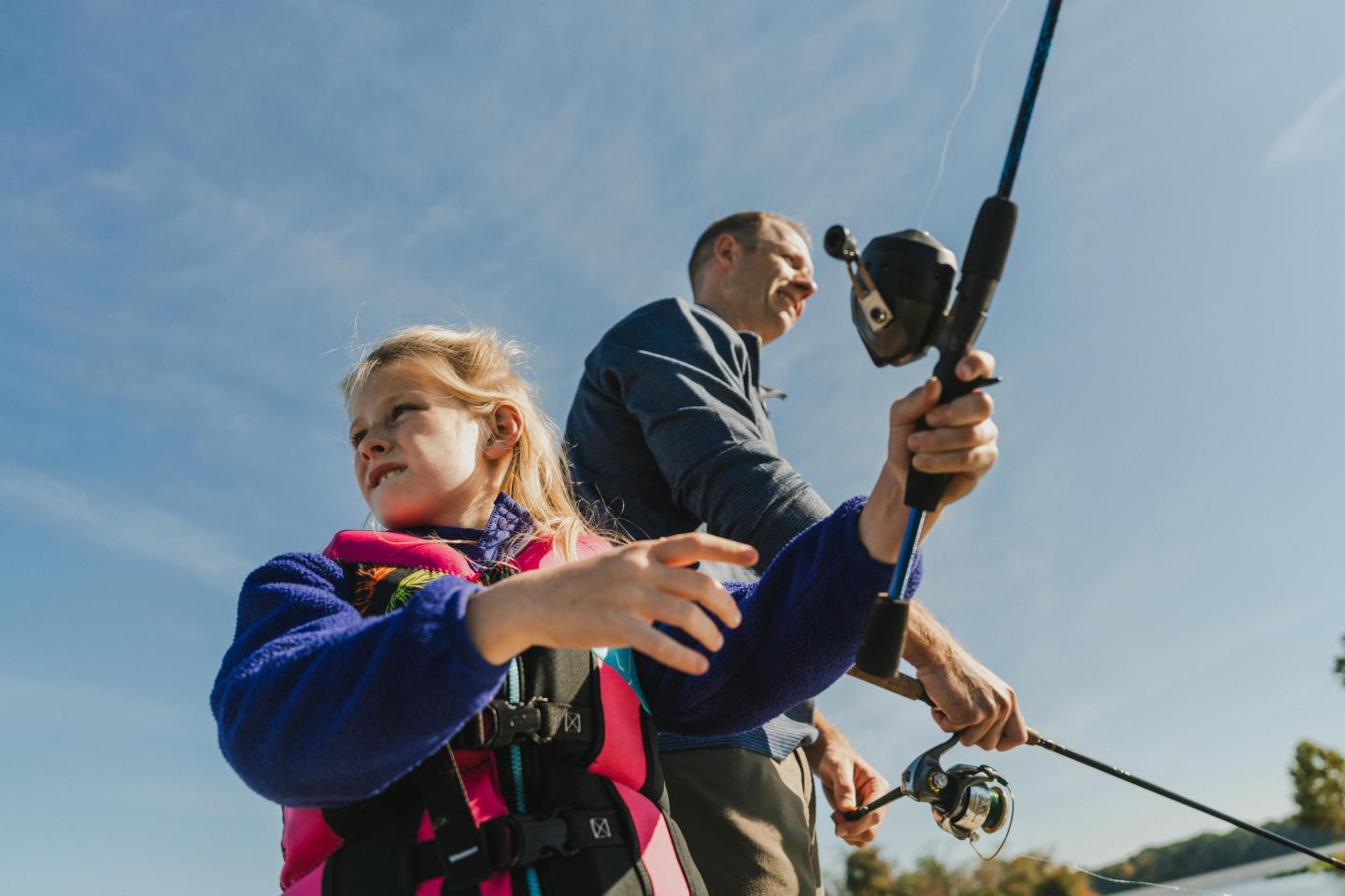 Child and adult fishing under a clear blue sky.